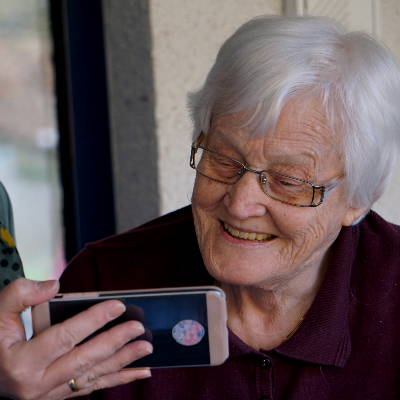 Senior citizen smiles as she watches a video on a cellphone